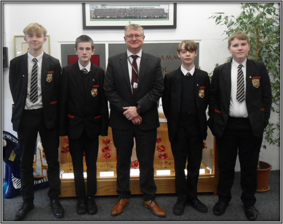 a group of students in school uniform with the Headteacher accepting their award
